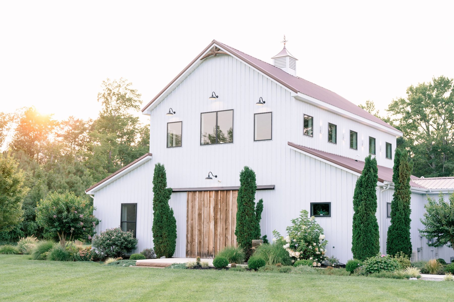 The white barn at Wildflower Estate at golden hour, with sliding wood doors, cypress trees and landscaped beds