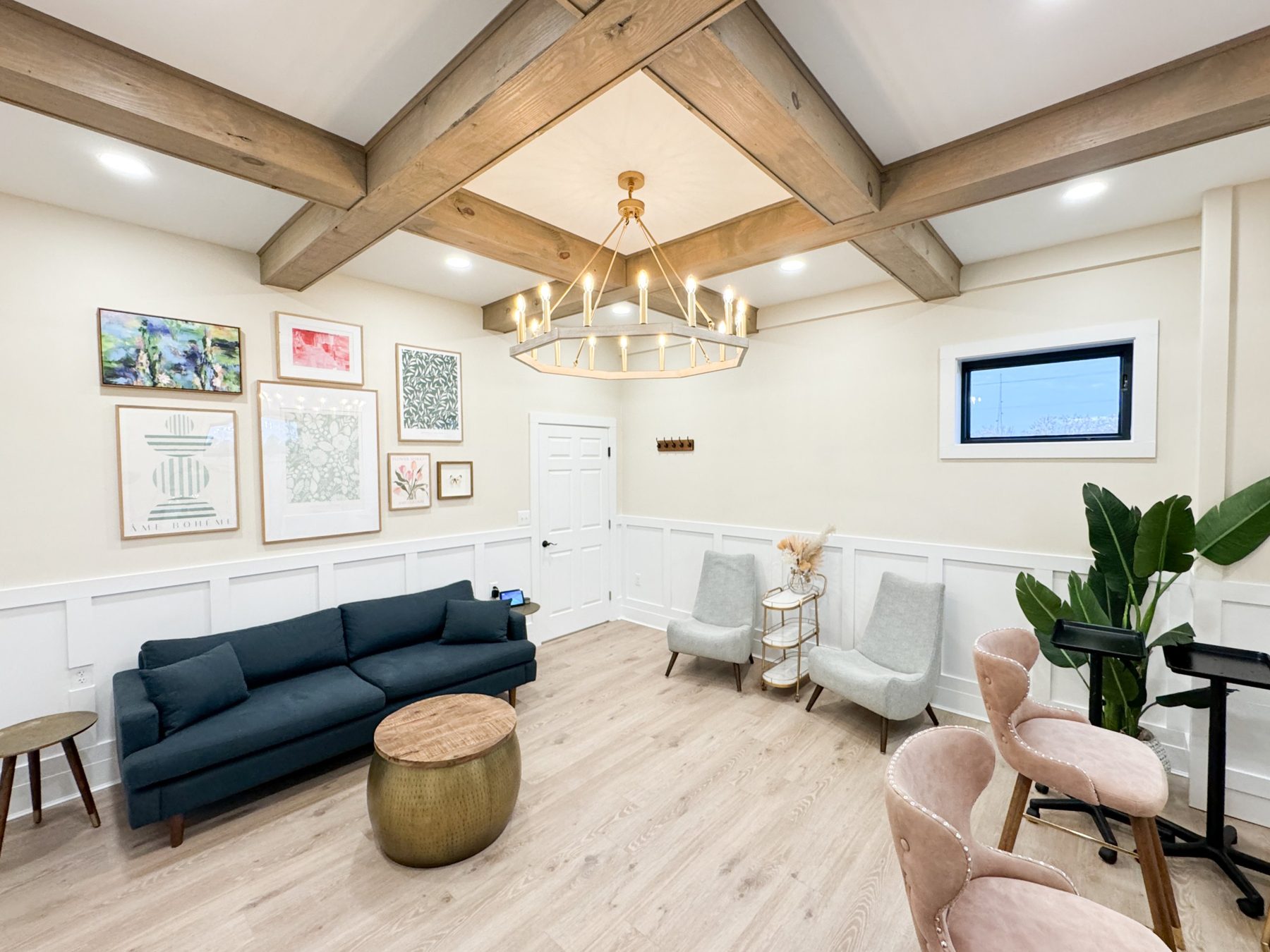 The bridal suite: a gallery wall, navy sofa and brass drum table under wood ceiling beams and a candle chandelier, with blush makeup chairs